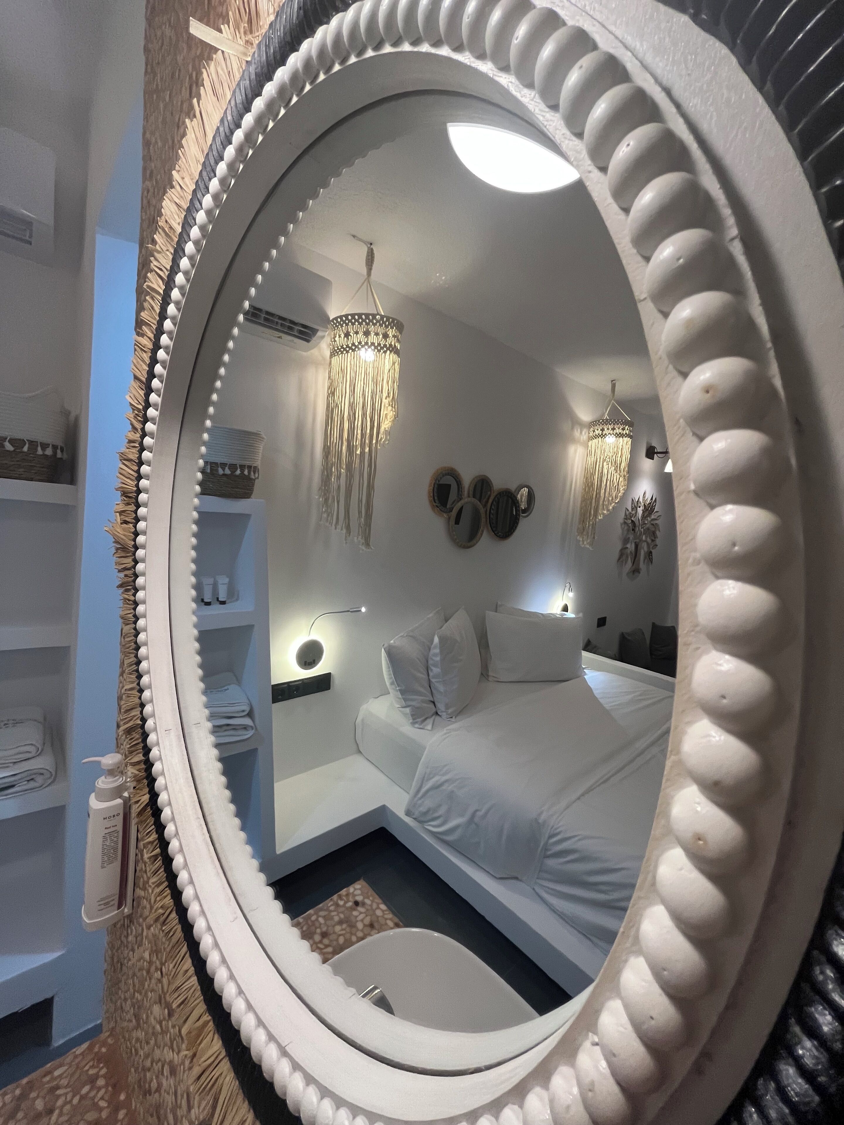 A bedroom with a large mirror, a bed, a bedside table, a nightstand, and a hanging light fixture.