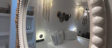 A bedroom with a large mirror, a bed, a bedside table, a nightstand, and a hanging light fixture.