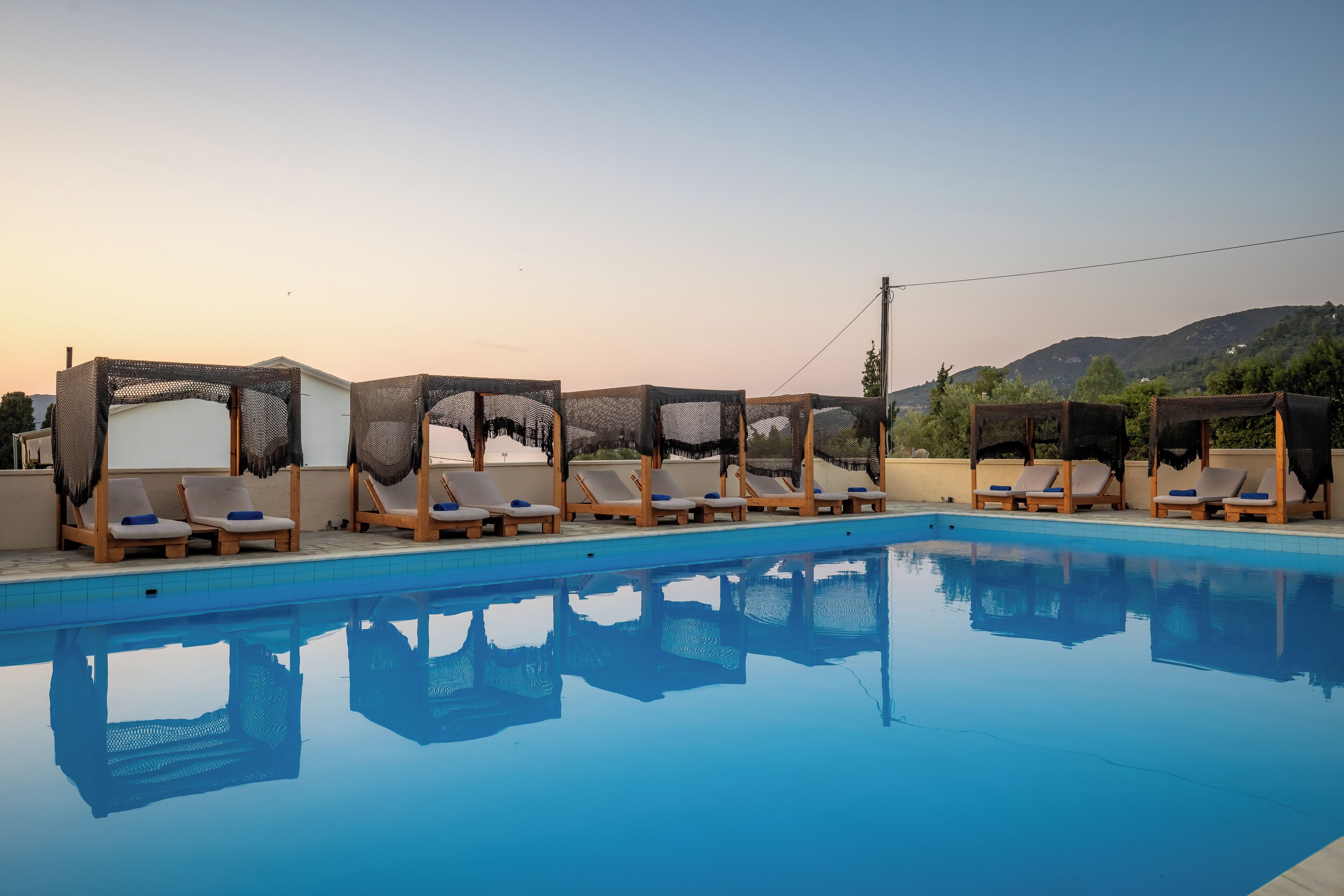 A swimming pool with lounge chairs and sunshades, surrounded by a clear sky and distant hills.