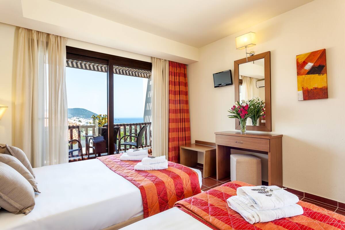 Habitación de hotel con dos camas, televisión, espejo y balcón con vistas.