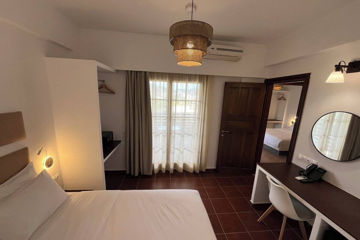 A hotel room with a bed, desk, chair, and a large mirror.