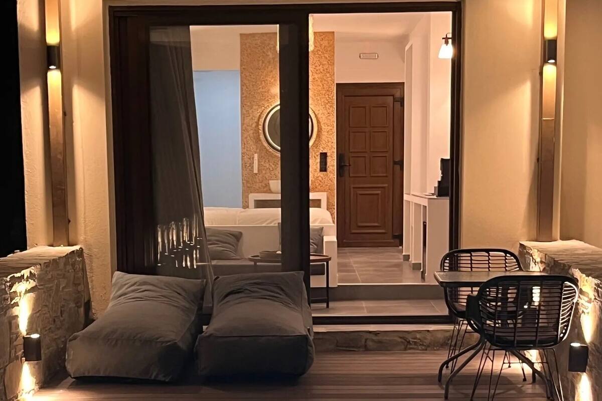A modern indoor swimming pool with a wooden deck, a sofa, and a dining area with chairs.