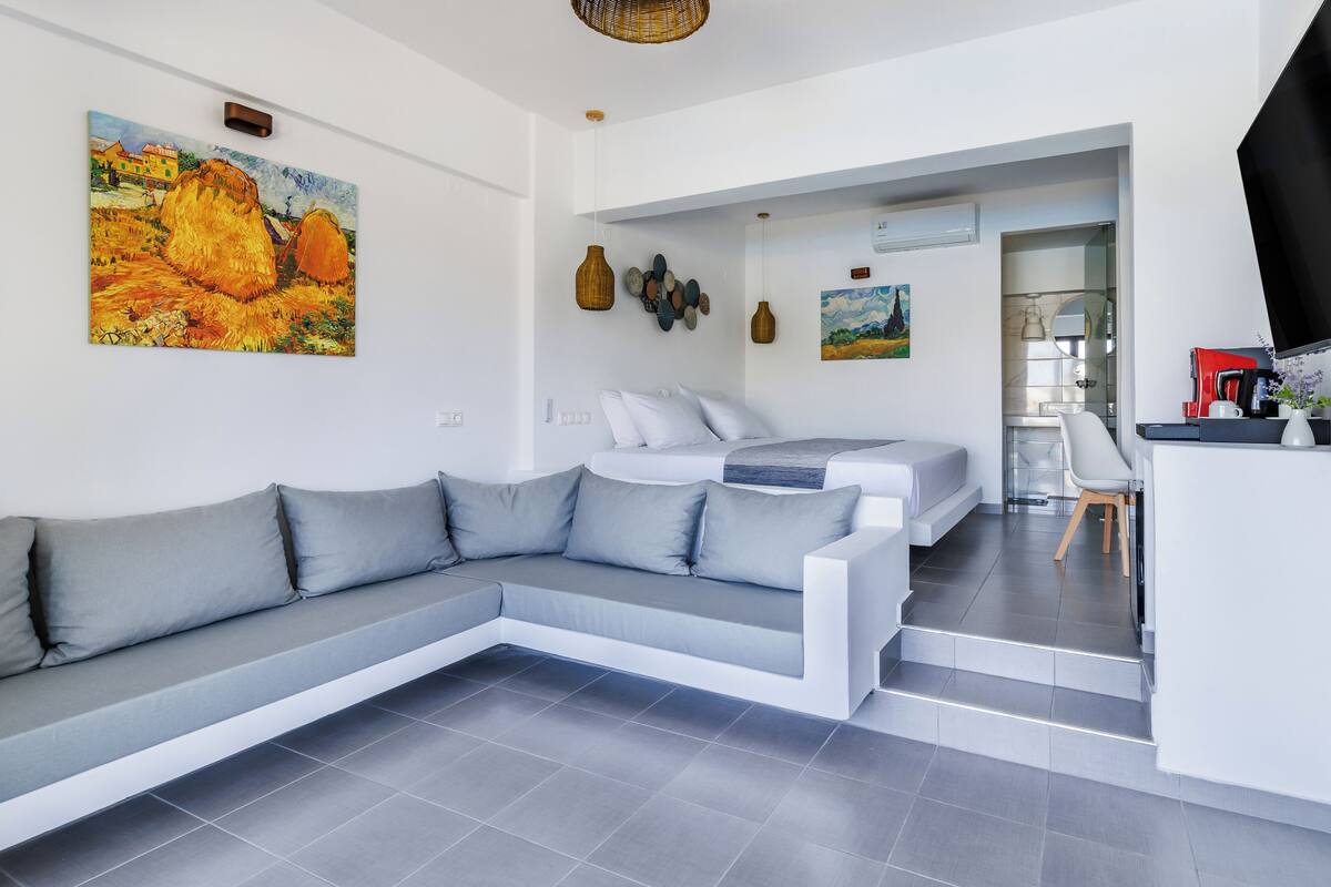 Una sala moderna con un sofá modular gris, una cama y una zona de cocina.