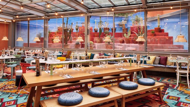 A restaurant with wooden tables, benches, and colorful patterned carpet. - Mama Shelter Marseille (Marseille)