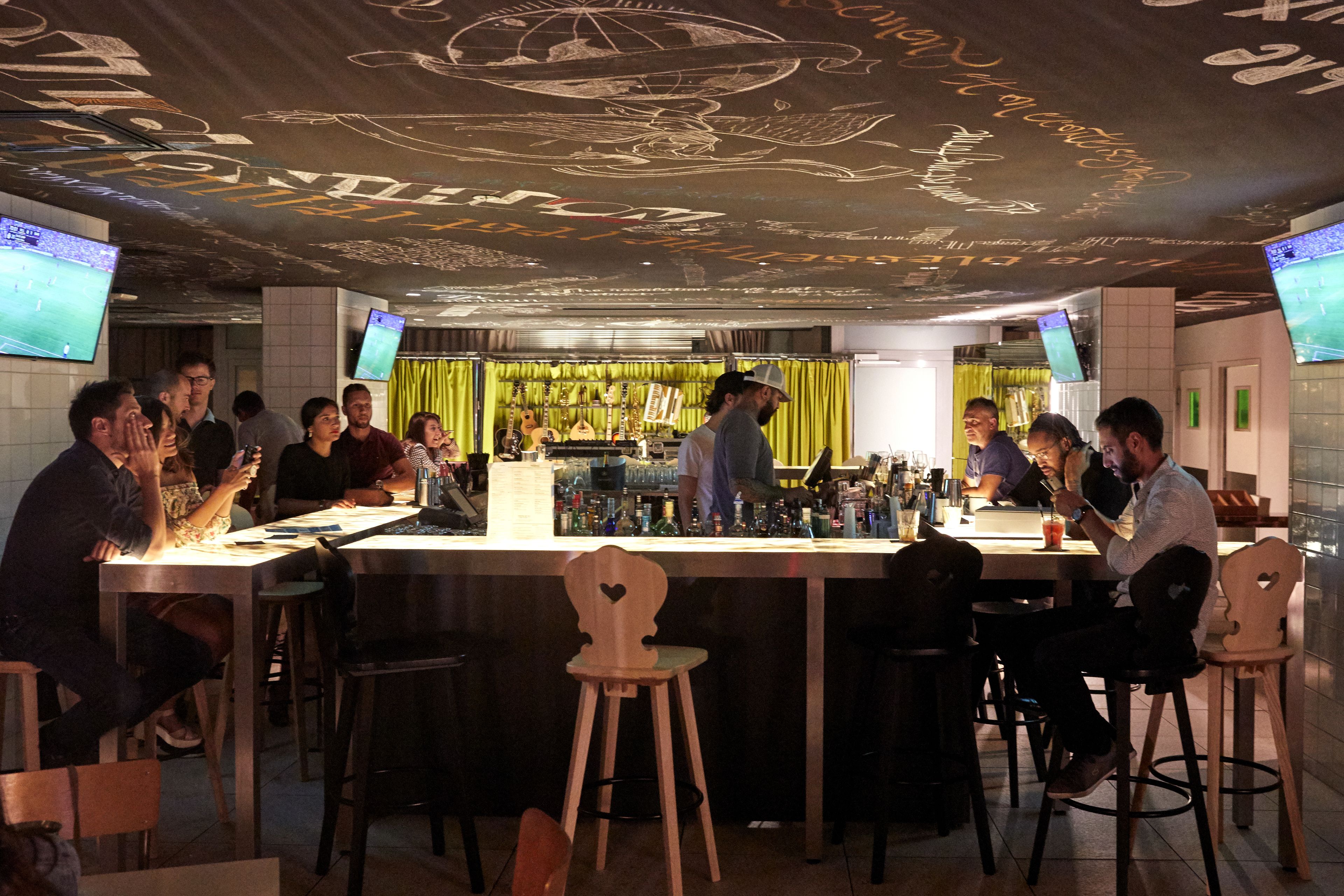 Zona de bar con mostrador, taburetes y un grupo de personas.
