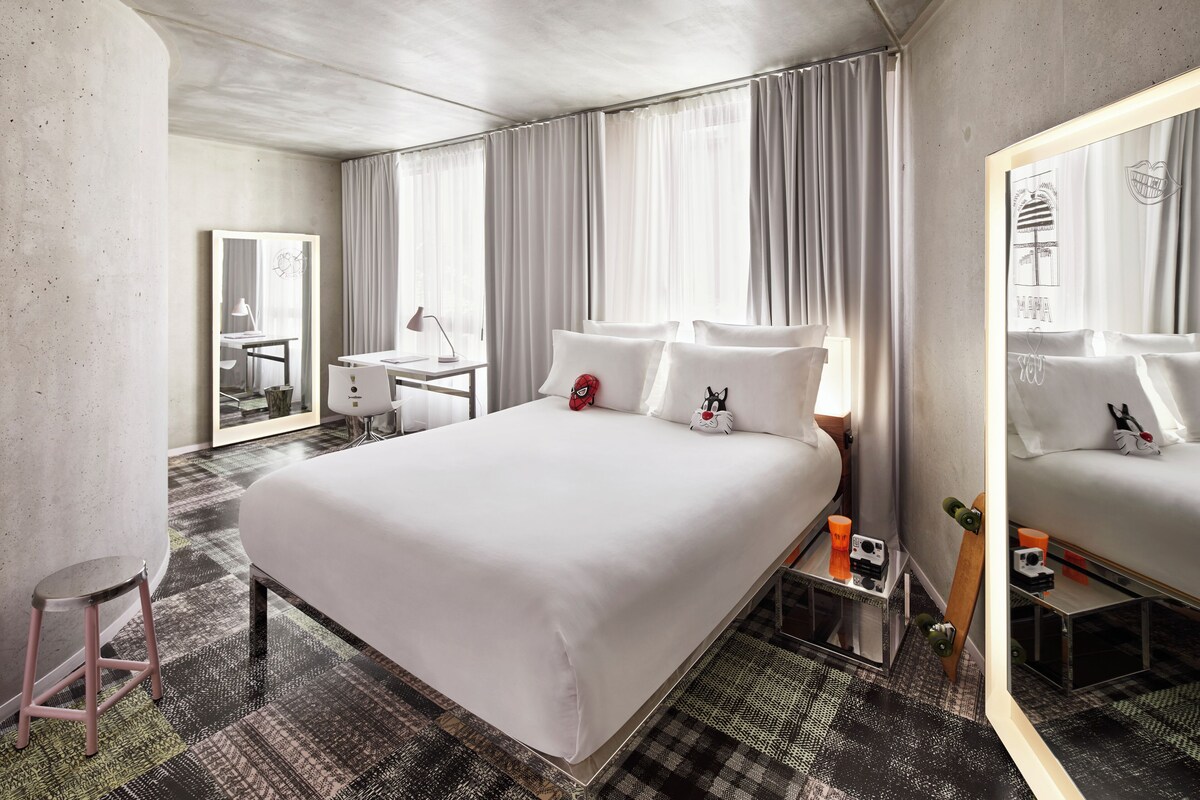 Une chambre d’hôtel avec un grand lit, un bureau, une chaise, un miroir et un tapis à motifs.