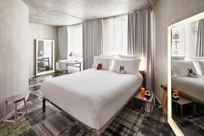 Hotelkamer met een groot bed, een bureau, een stoel, een spiegel en een kamerbreed tapijt met een patroon.