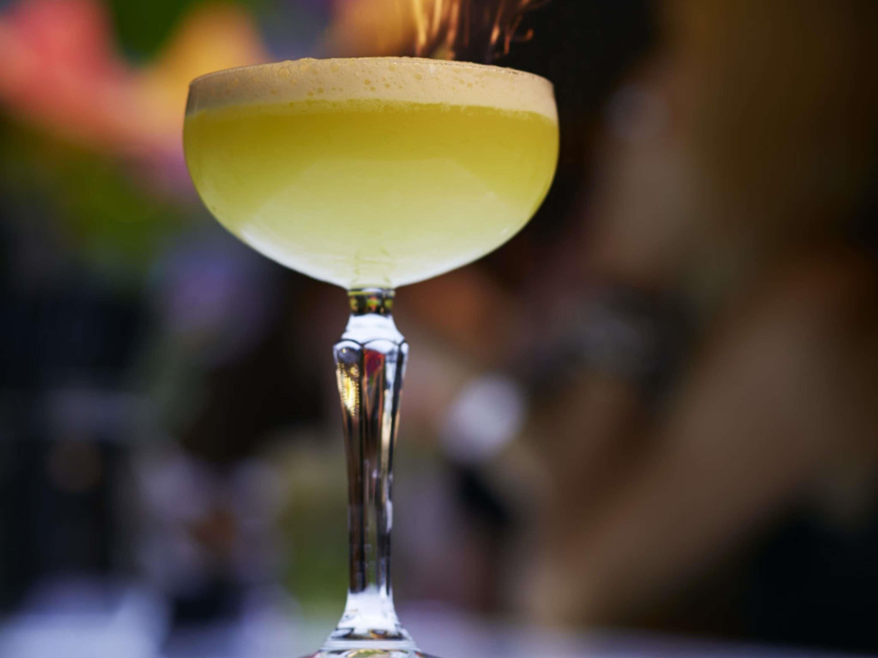 A cocktail glass with a frothy top, placed on a reflective surface.