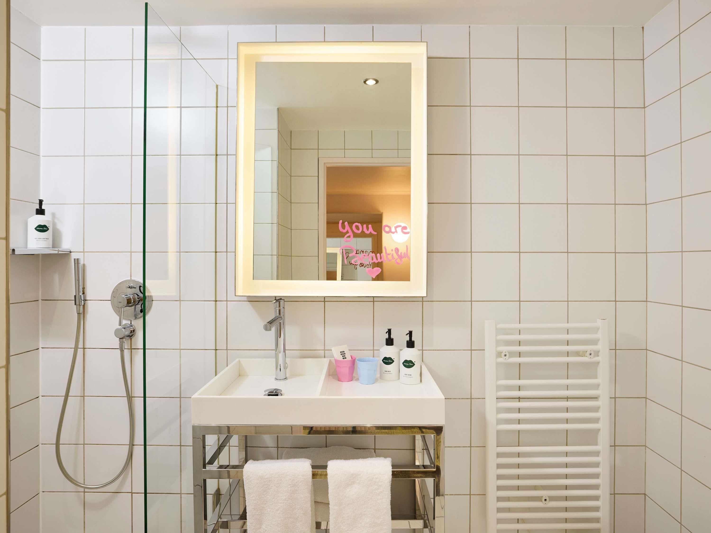 Une salle de bain avec un miroir, un lavabo, un porte-serviettes et une douche.