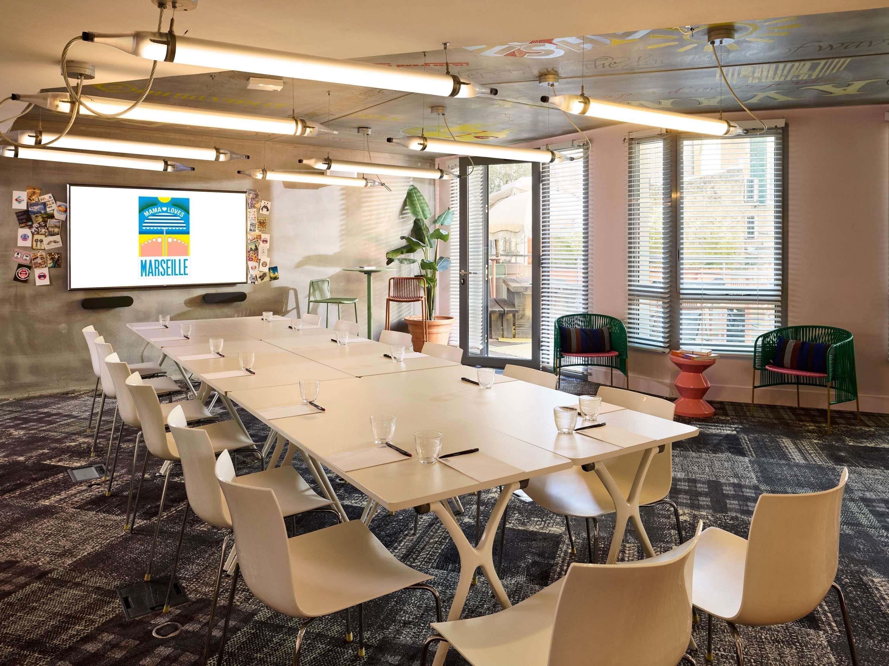 A conference room with a long table, chairs, a projector screen, and a large window with blinds.