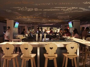 A bar area with wooden chairs, a bar counter, and a ceiling with decorative writing. - Mama Shelter Marseille (Marseille)