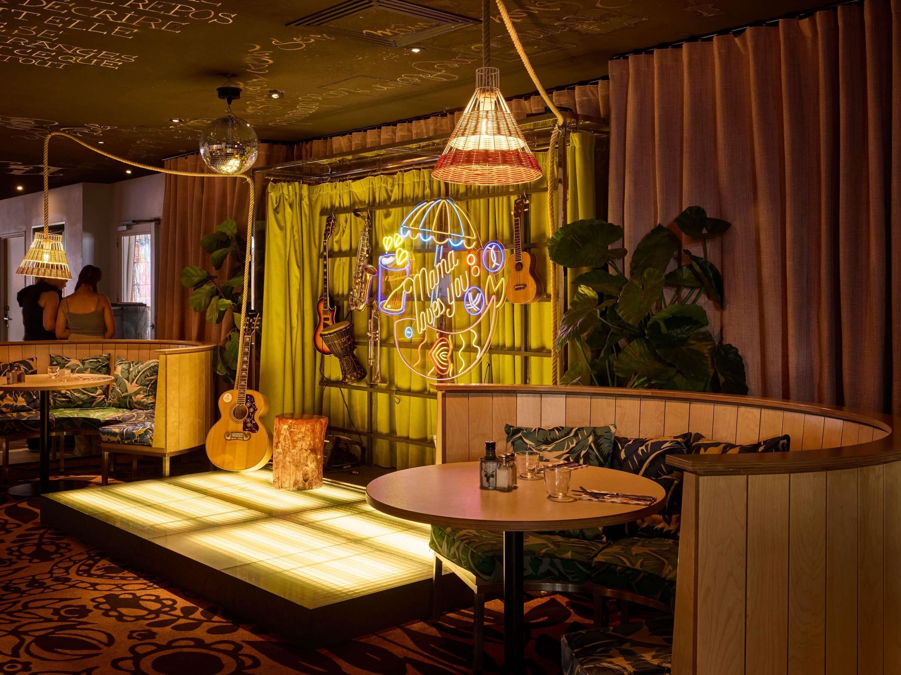 A cozy room with a green curtain backdrop, a neon sign, and a variety of musical instruments.