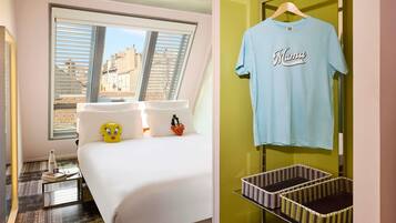 A hotel room with a bed, pillows with cartoon characters, a window with blinds, and a wall-mounted basket shelf.