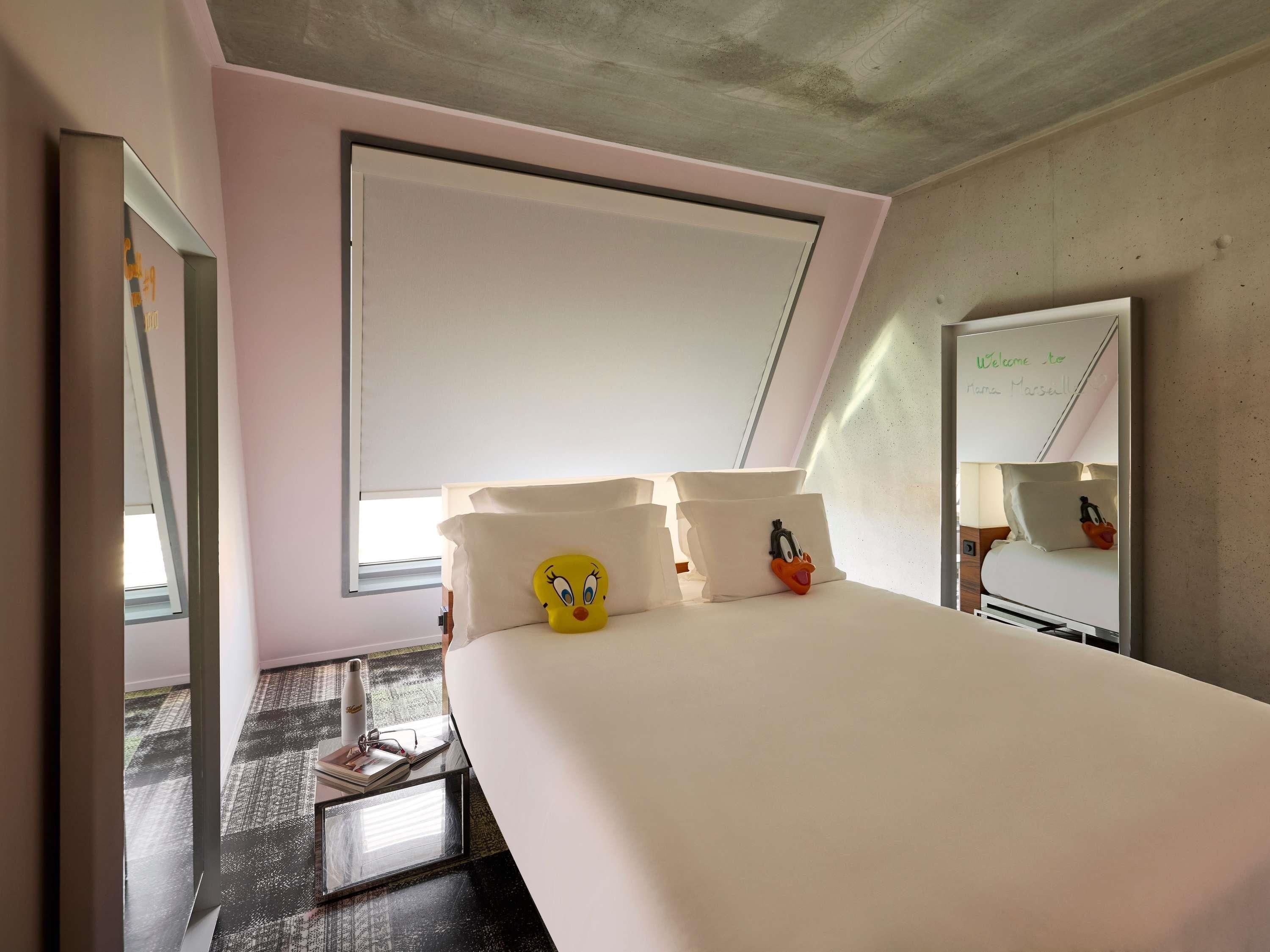 Une chambre d’hôtel avec un grand lit, une fenêtre, un miroir et un panneau d’accueil.
