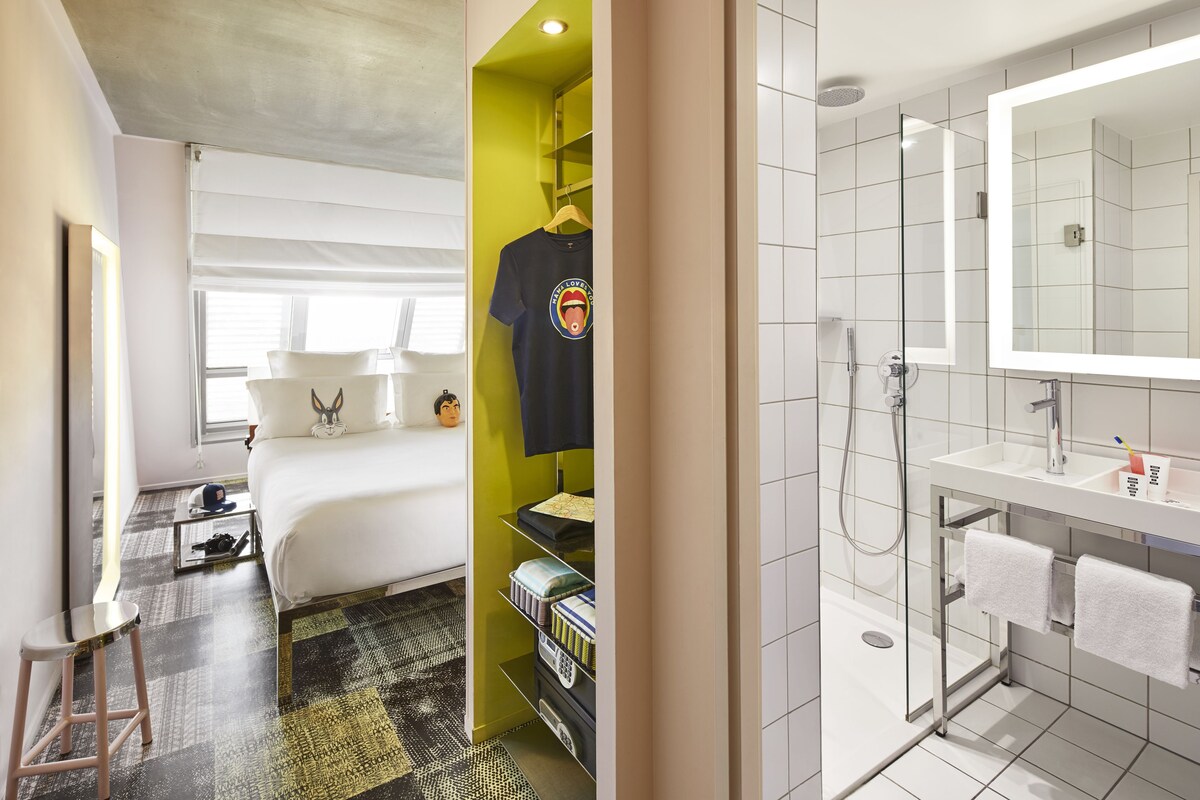 Une chambre d’hôtel comprenant un lit, une armoire, une salle de bain avec un miroir et une douche.