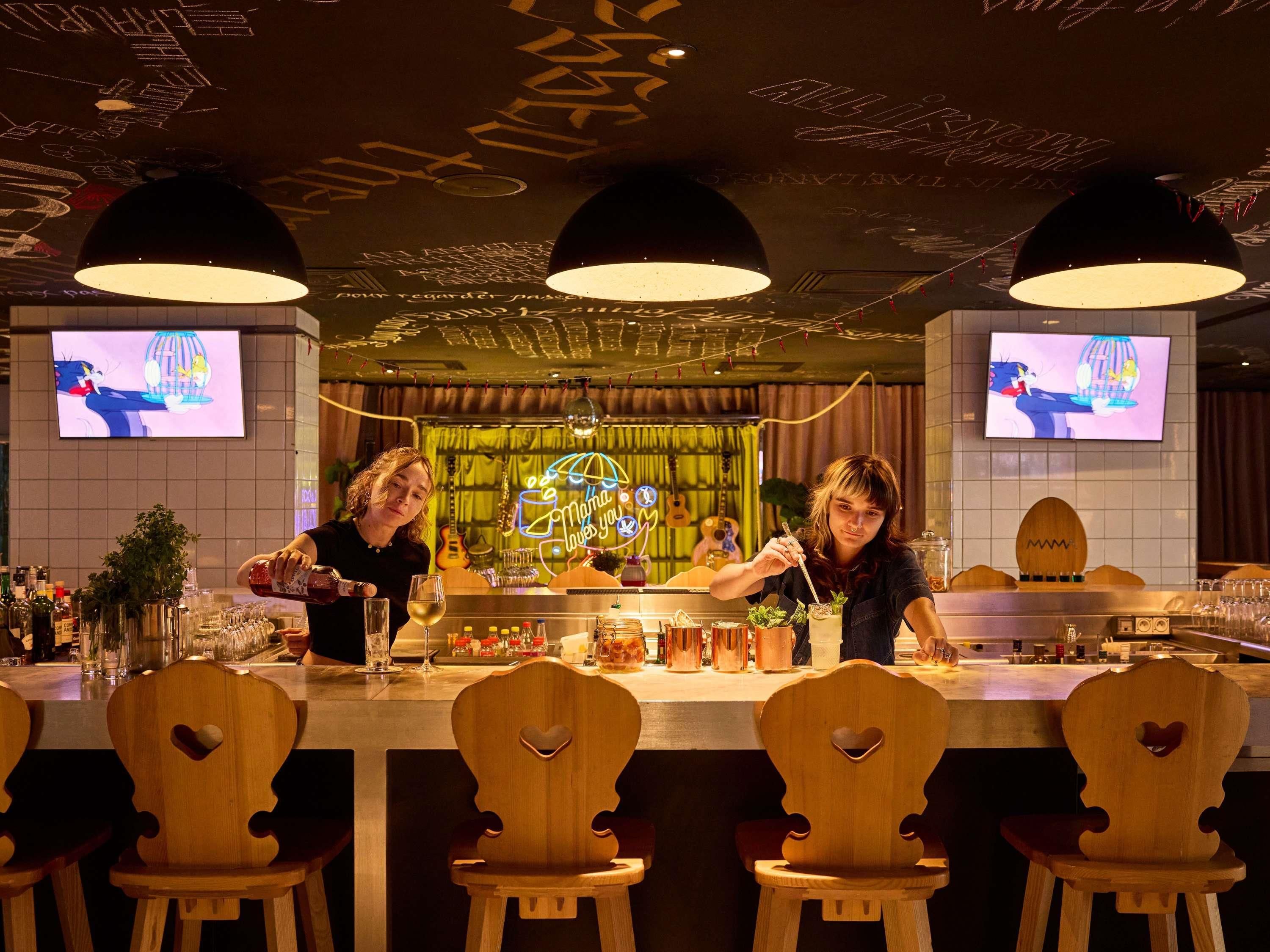A bar area with wooden chairs, a counter, and two televisions displaying cartoons.