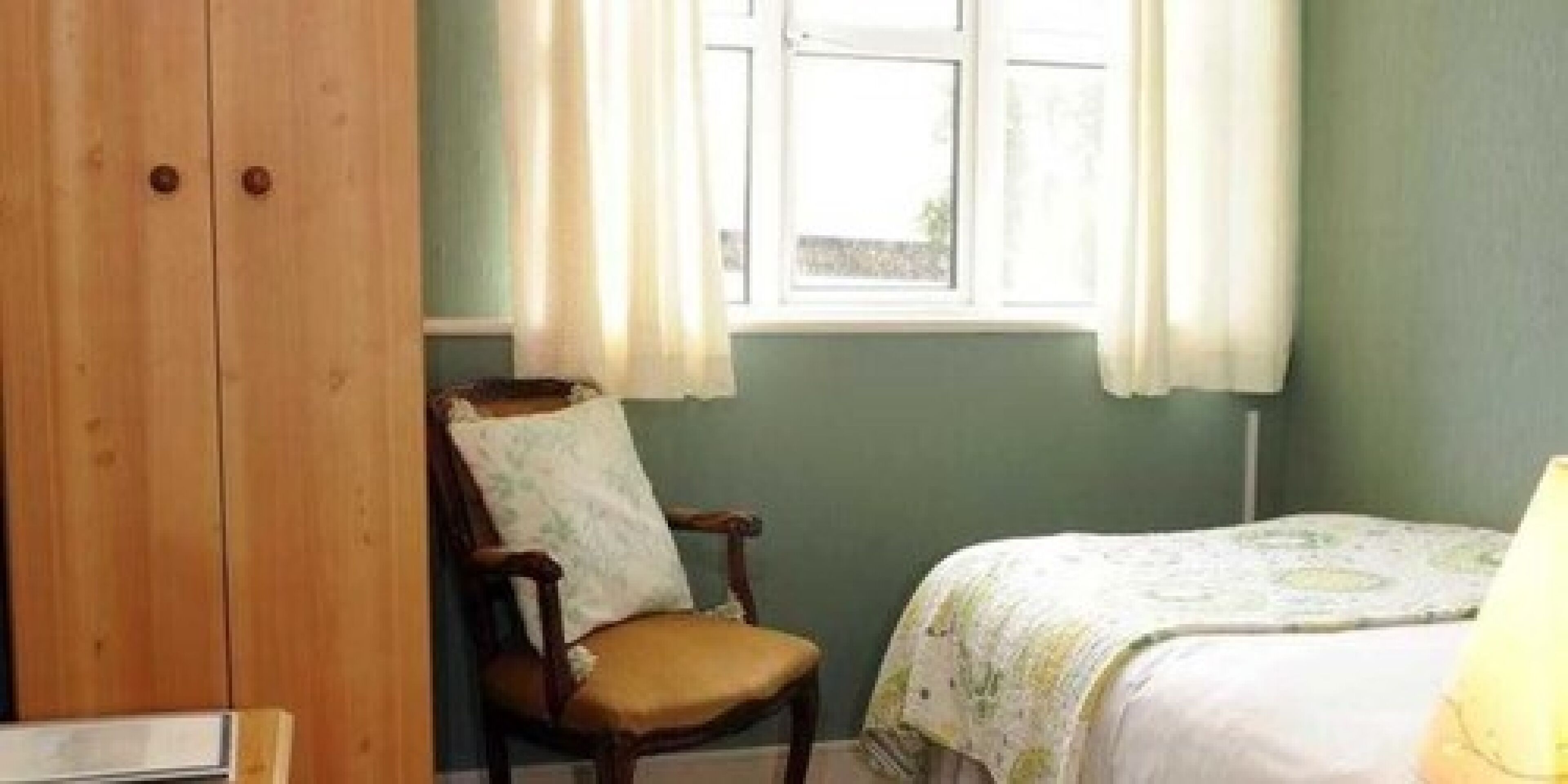 A room with a bed, a chair, and a wooden wardrobe.