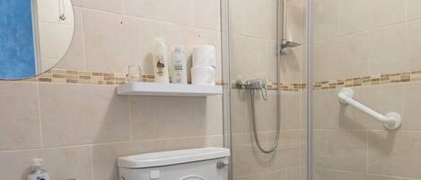 Un baño con inodoro, lavamanos y cabina de ducha con mampara de vidrio.