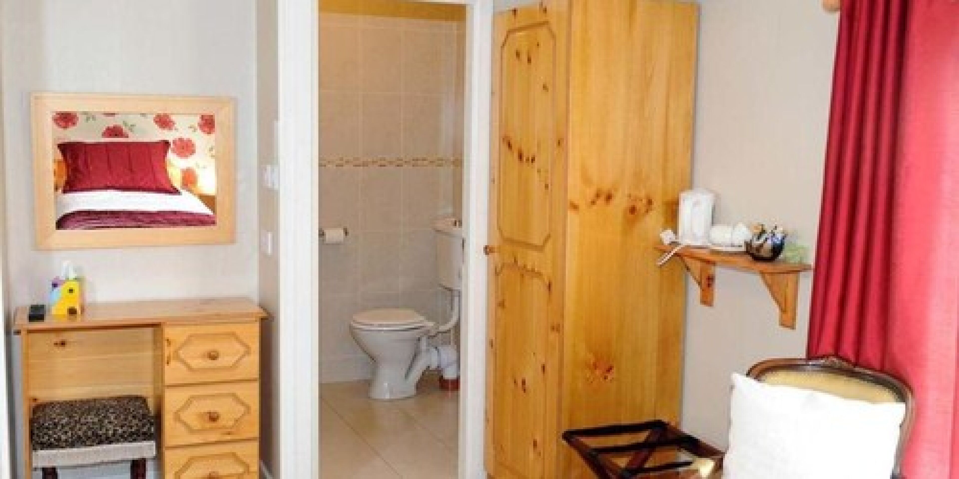 A bedroom with a bed, a wooden dresser, a framed picture, and a bathroom with a toilet and shower.