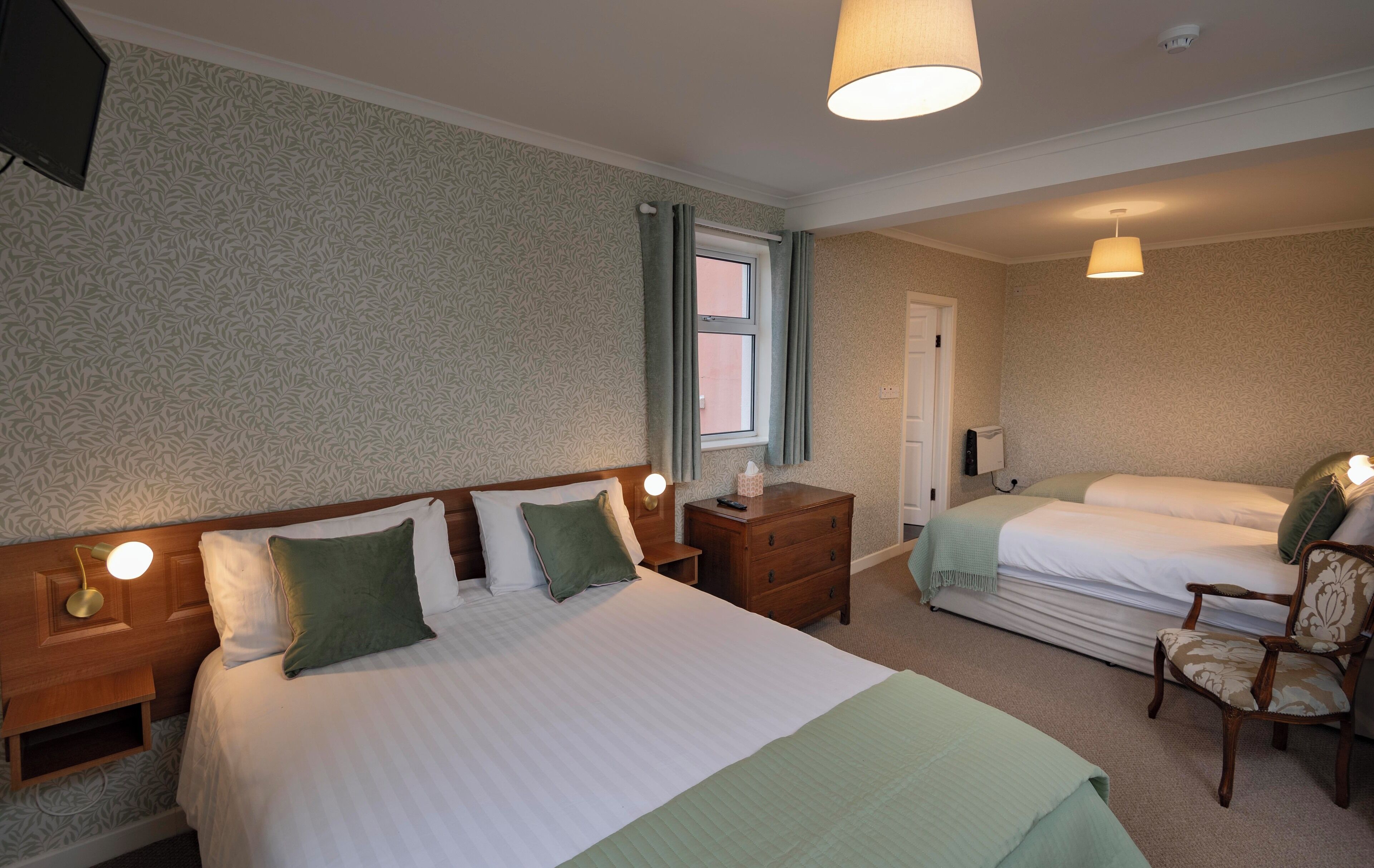 A hotel room with a large bed, a smaller bed, a nightstand, a chair, and a window.