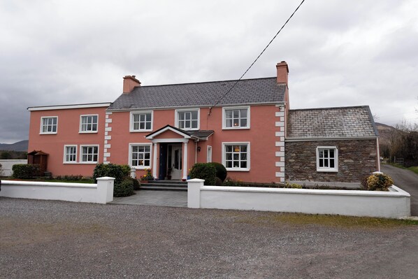 A two-story house with a red facade and white trim, featuring a front porch and a stone extension. - Murphy's Farmhouse (Castlemaine)