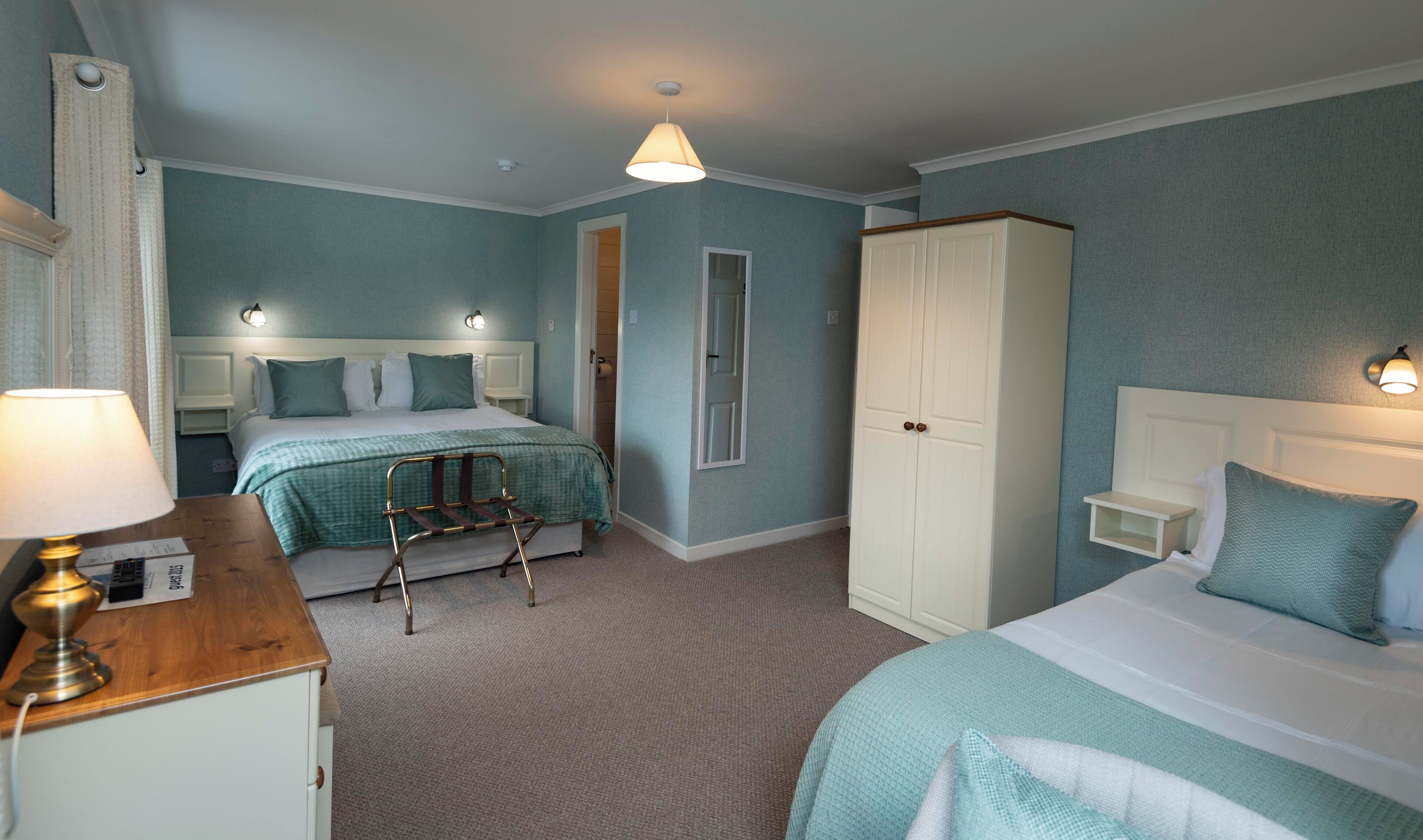 A hotel room with two beds, a wardrobe, a bedside table, and a lamp.