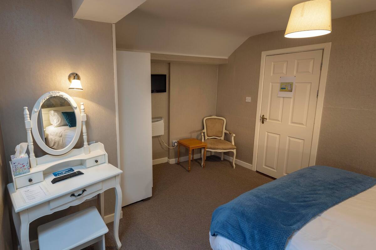 A hotel room with a bed, a vanity with a mirror, a chair, and a door.