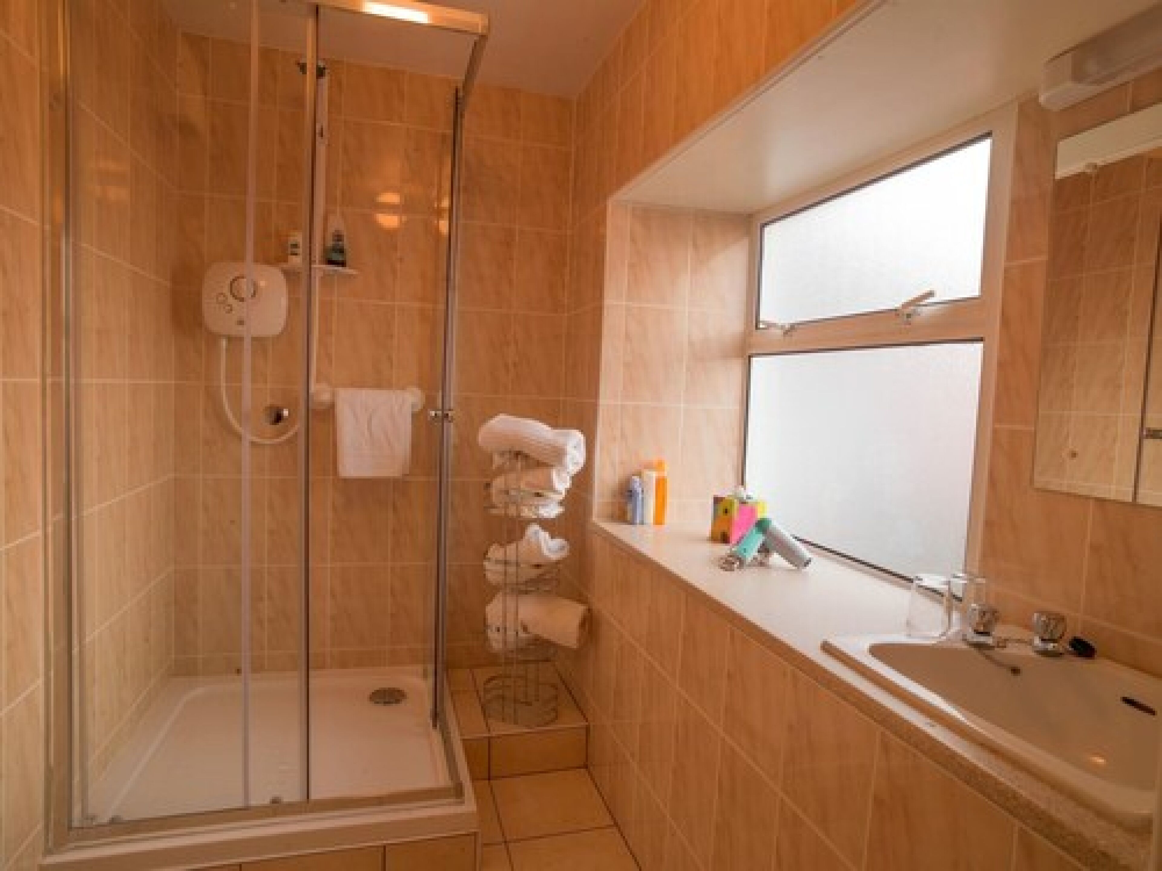 Un baño con ducha de vidrio, un lavamanos y una ventana.