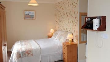 A bedroom with a bed, two bedside lamps, a wooden nightstand, a wall-mounted shelf with a radio, and a framed picture on the wall.