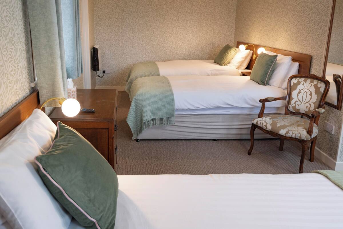 A hotel room with two beds, a nightstand with a lamp, a chair, and a mirror.