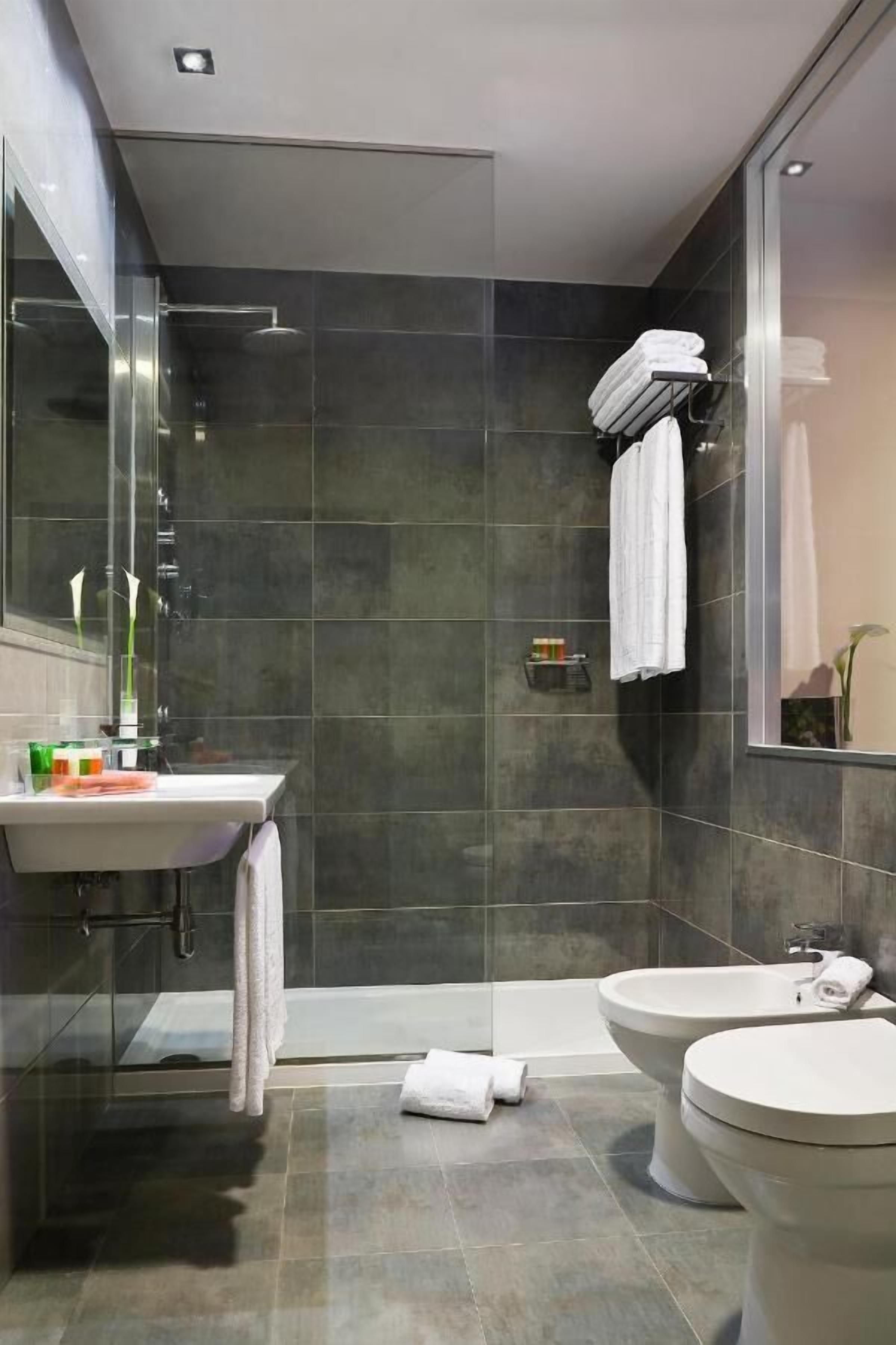 Et moderne badeværelse med brusekabine i glas, håndvask med toiletartikler, en bidet og et toilet.