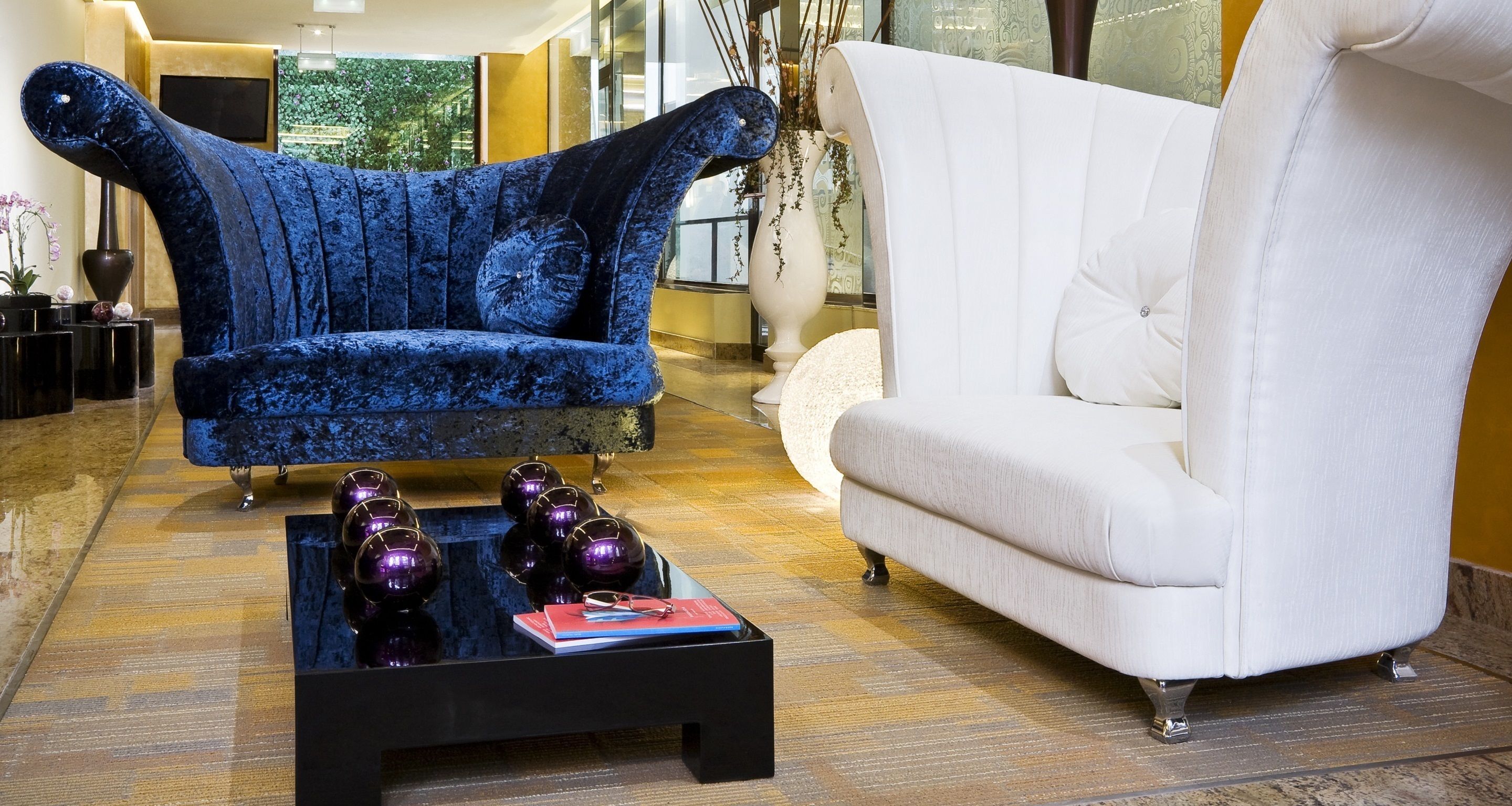 A modern living room with a blue velvet armchair, a white sofa, and a black coffee table with decorative items.