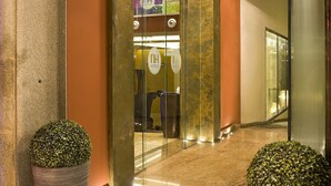 A hotel entrance with a glass door, a potted plant, a decorative ceiling light, and a reception area visible through the glass. - NH Ourense (Ourense)