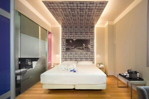 A modern hotel room with a large bed, a glass-enclosed bathroom, and a tufted ceiling.