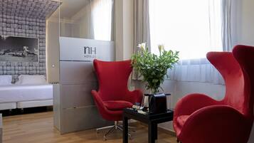 A hotel room with a bed, two red armchairs, a small table with a vase of flowers, and a sign reading "nh hotels".