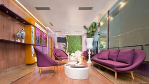 A modern lobby with wooden flooring, purple seating, a round coffee table, and a green wall with plants. - NH Ourense (Ourense)