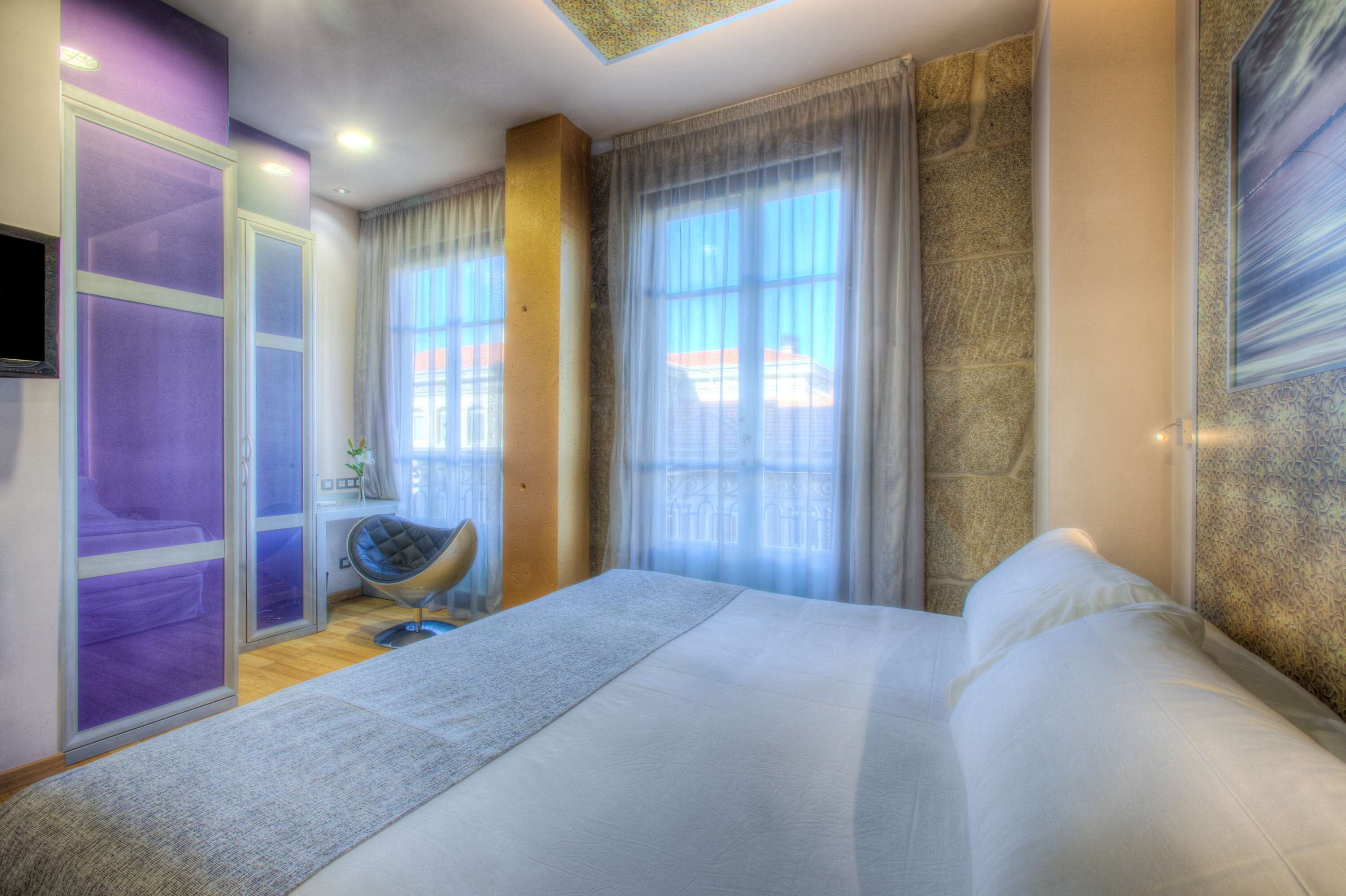 Habitación de hotel con una cama grande, una silla, un televisor y una ventana con cortinas.
