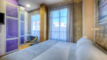 Habitación de hotel con una cama grande, una silla, un televisor y una ventana con cortinas.