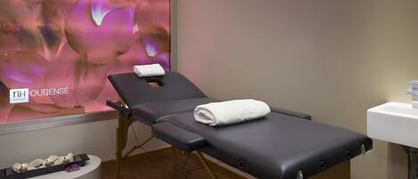 A treatment room with a massage table, a sink, and a decorative wall with a floral pattern.