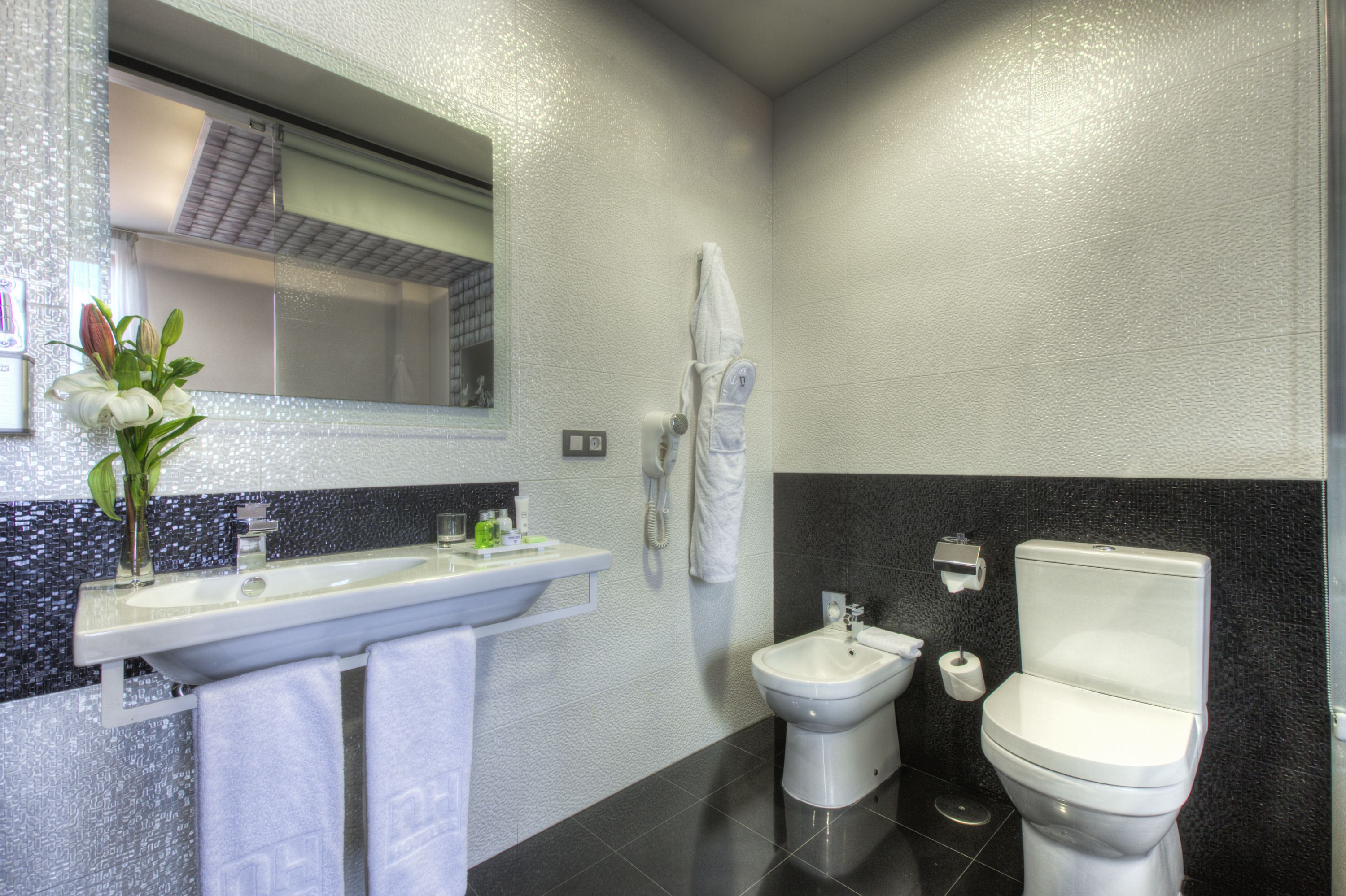 A modern bathroom with a large mirror, a sink, a bidet, and a toilet.
