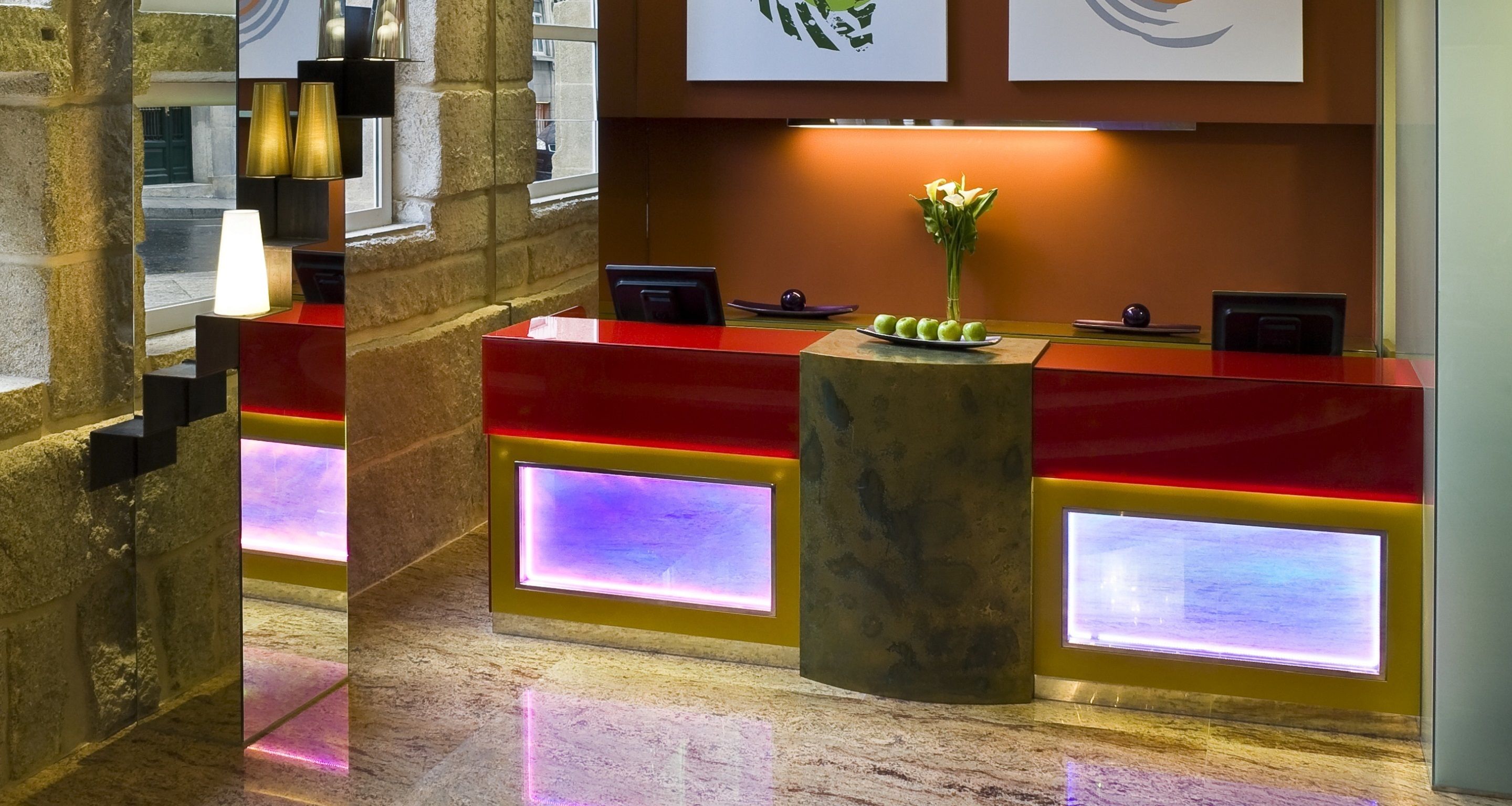 A hotel reception desk with a red and yellow color scheme, a vase of flowers, and illuminated panels.