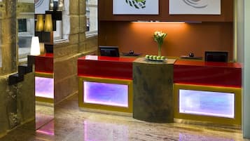 A hotel reception desk with a red and yellow color scheme, a vase of flowers, and illuminated panels.