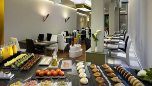 A modern hotel dining area with a buffet setup, including various food items and a seating arrangement. - NH Ourense (Ourense)