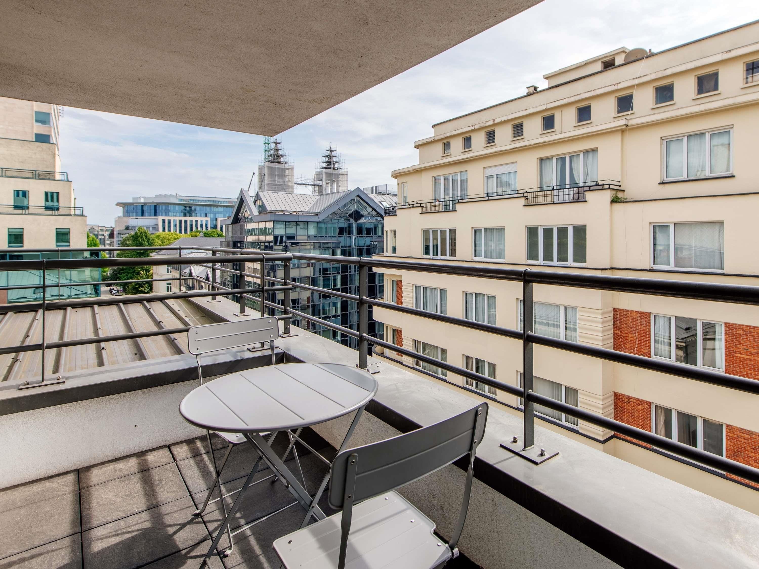 Un balcon avec une table et des chaises, donnant sur un paysage urbain composé d’immeubles et d’un chantier de construction.