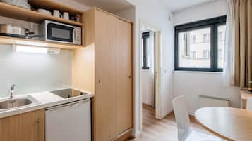 Een compacte keuken met een magnetron, spoelbak en kastjes. Er is een eethoek met een tafel en stoelen.
