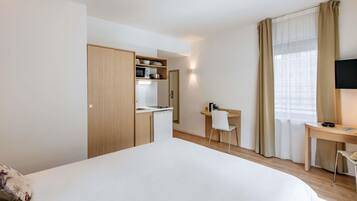 Hotelkamer met een bed, bureau, stoel, kitchenette en televisie.