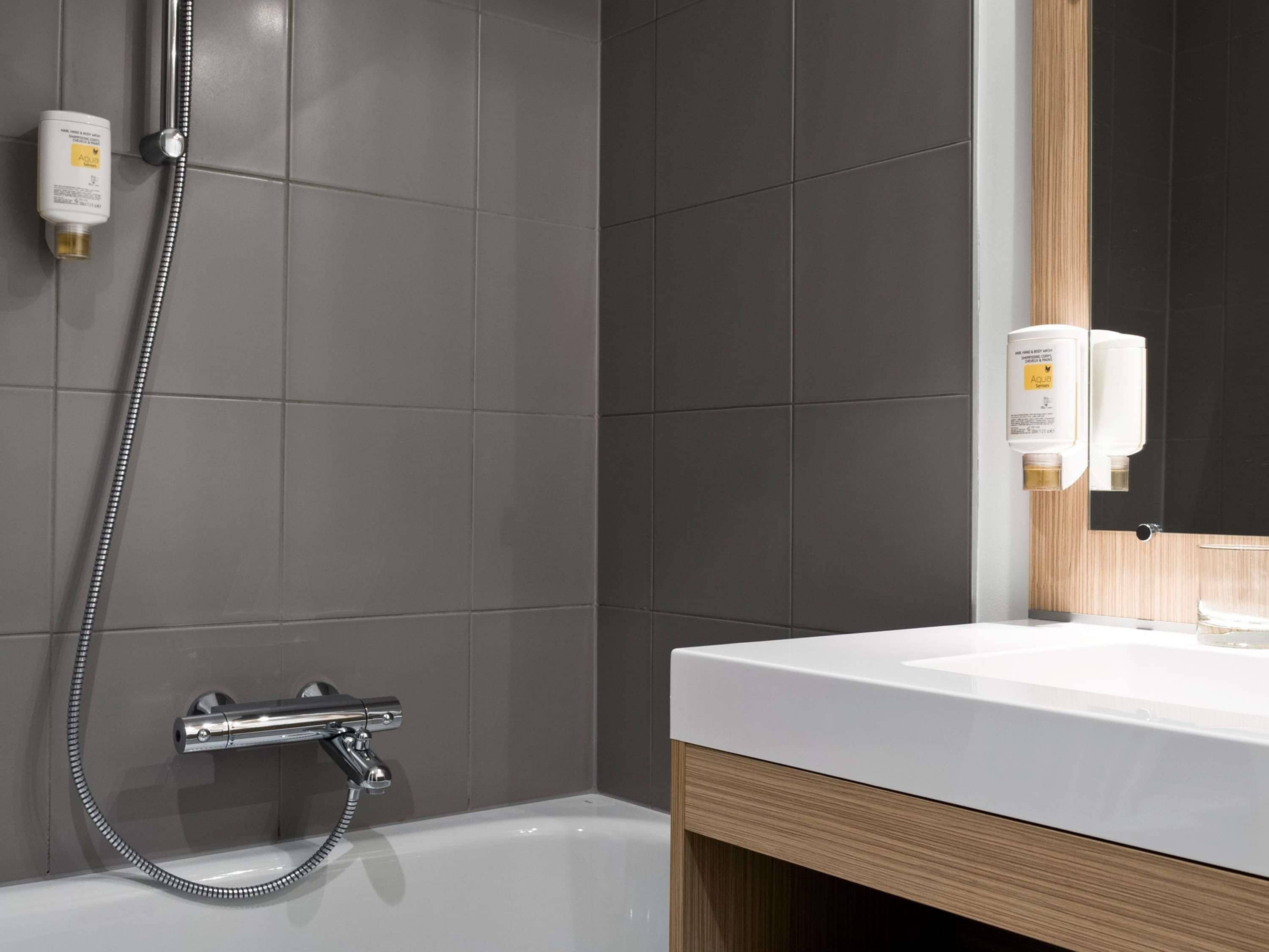 A modern bathroom with a bathtub, a shower with a handheld hose, and two bottles of shampoo on the wall.