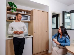 Cocina compacta con microondas, refrigerador pequeño y un armario con vajilla.