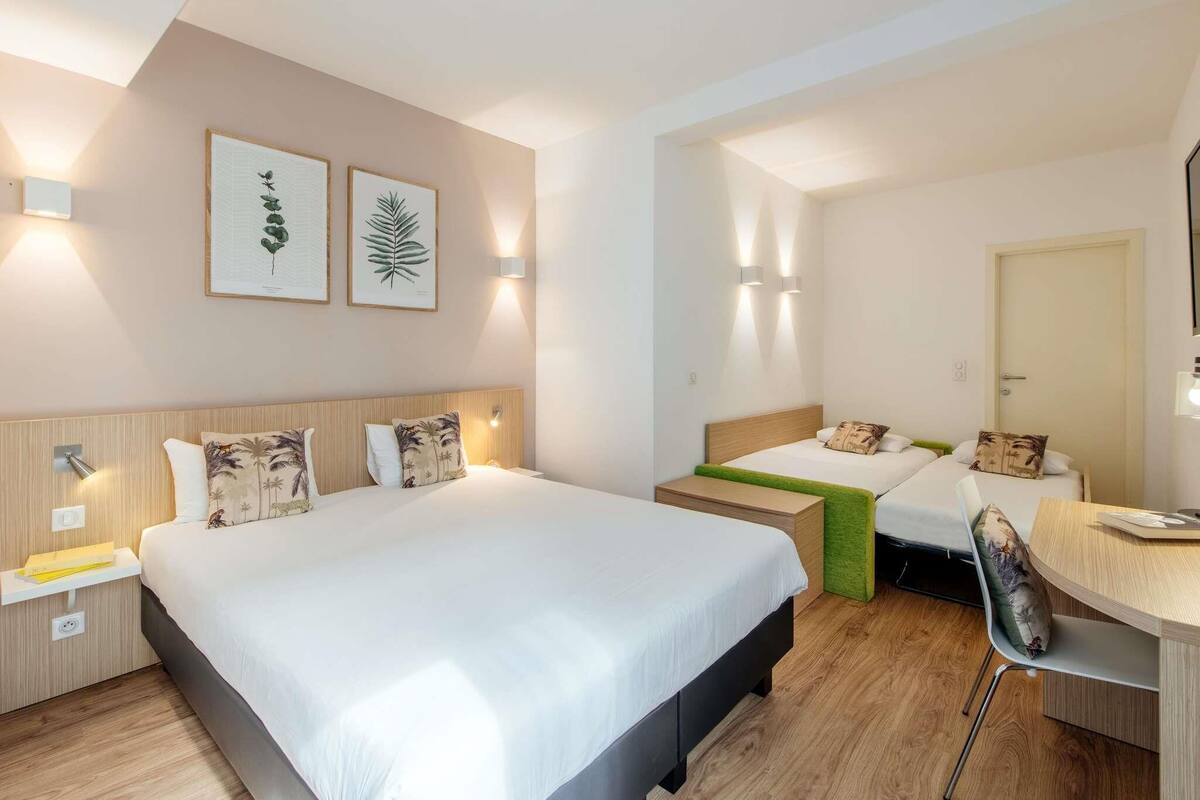 Habitación de hotel con dos camas, un escritorio y una silla. Tiene luces fijadas a la pared e impresiones botánicas enmarcadas.