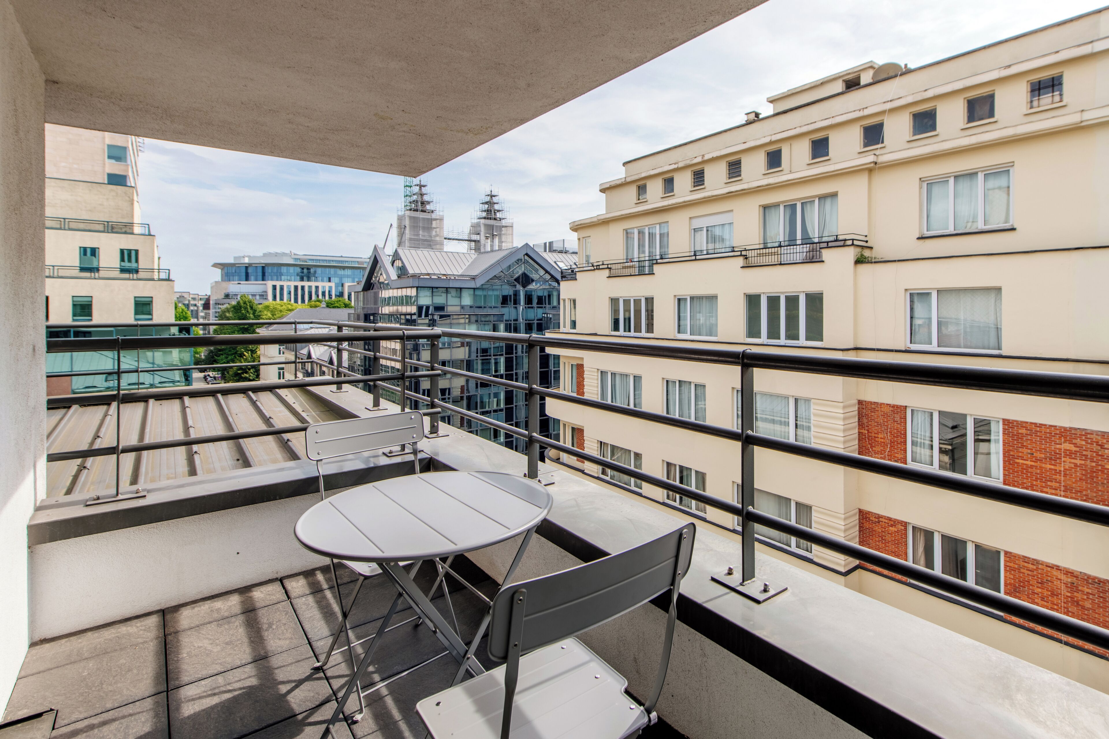 Un balcón con mesa y sillas, con vistas a un paisaje urbano que combina edificios modernos y tradicionales.